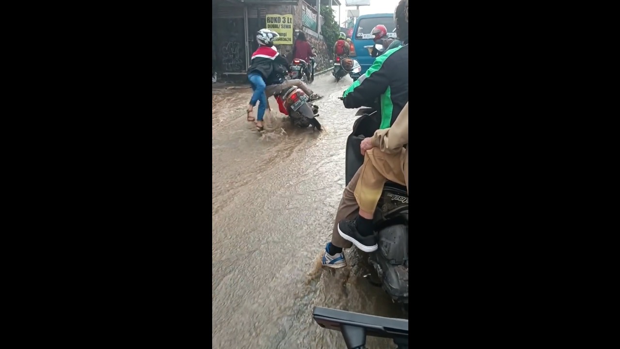 Perilous plunge: men tumble from motorbike amidst flooded road in Depok, Indonesia