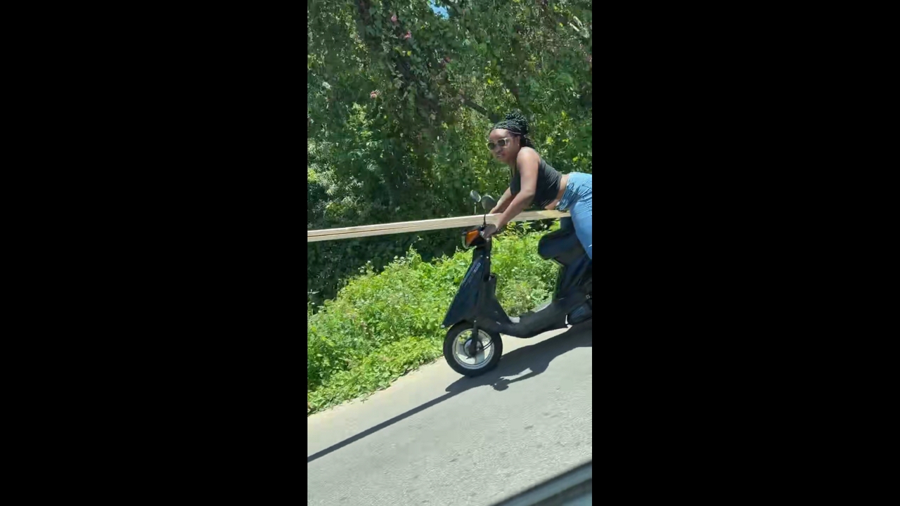 Woman rides motor scooter while carrying wood in Dajabón, Dominican Republic