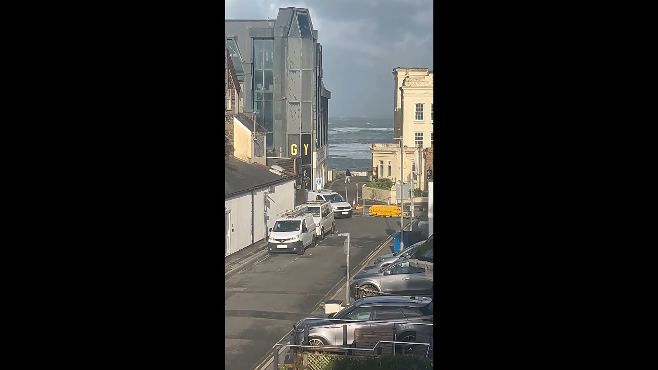 Man struggles to walk against strong winds during a coastal storm in Cornwall, UK