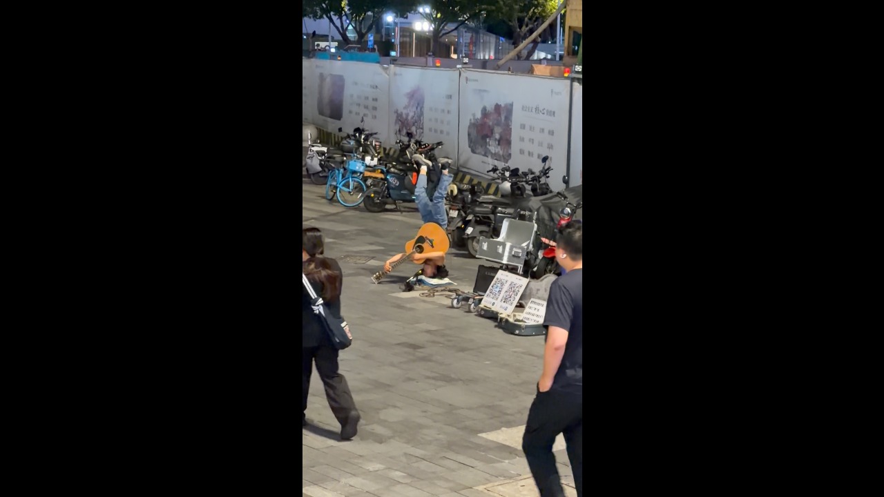 Street performer plays guitar while balancing upside down on a pillow in Guangzhou, China