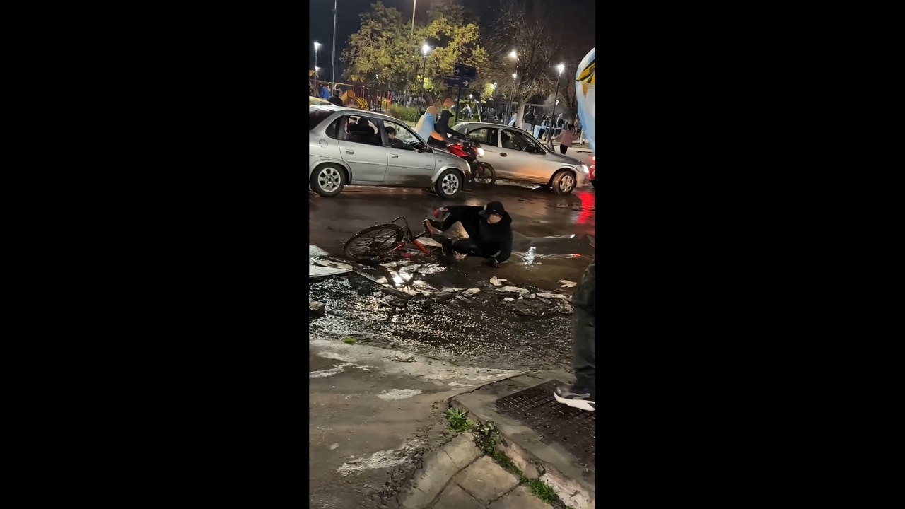 Cyclist slips in muddy puddle while crossing busy street in González Catán, Argentina