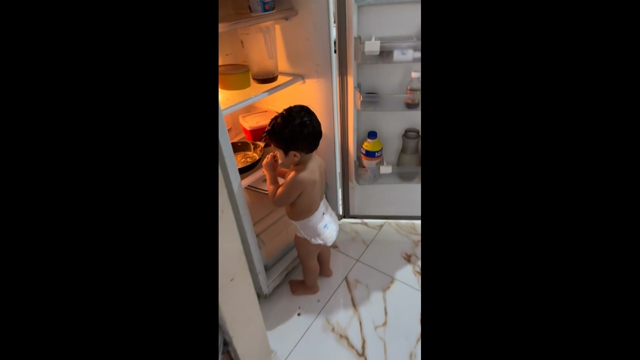 Toddler snacks from pan inside refrigerator in Oeiras do Pará, Brazil