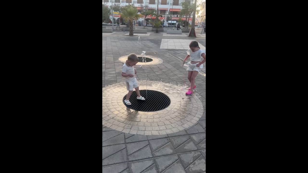 Children playfully splashed by water jets in Playa de las Américas, Spain