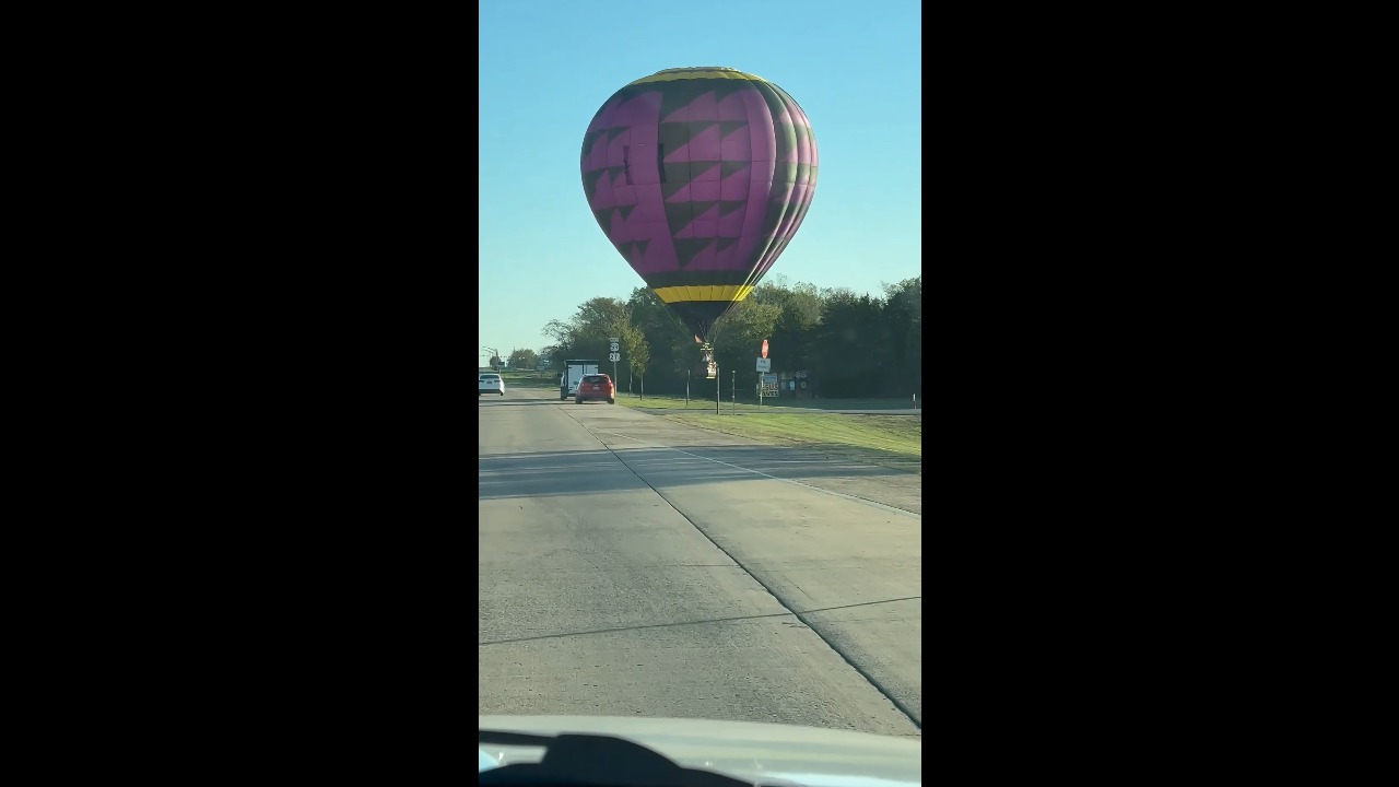 Low-flying hot air balloon drifts across a highway in Poteau, USA