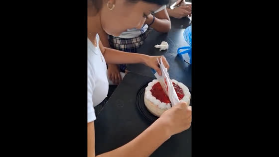 Lady cuts birthday cake with a ruler wrapped in notebook paper