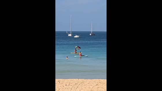 Man glides on surfboard holding umbrella at Nai Beach, Phuket, Thailand