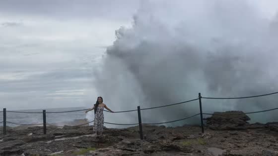 Woman gets splashed by wave on rocky shore in Lembongan Island, Bali, Indonesia