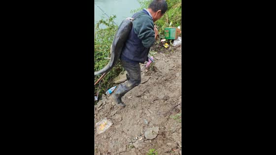 Man carries two fish up wet slope after fishing in Shaanxi, China