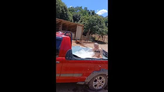 Grandfather and grandson turn car into improvised pool on a hot day in Alto Jequitibá, Brazil