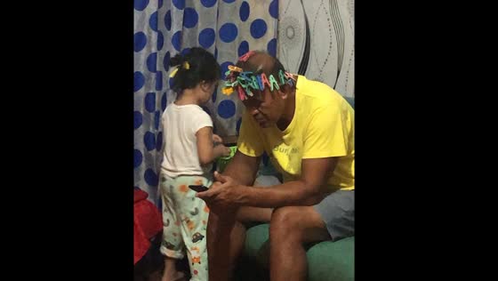 Child puts hair clips on grandfather's bald head in Manapla, Philippines