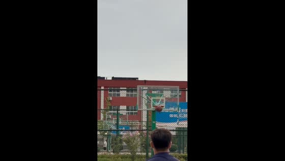 Man sinks long-distance basketball shot during children's practice in Henan, China