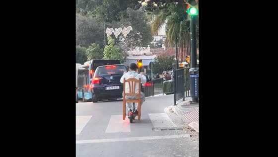 Person rides scooter while seated on attached chair in Málaga