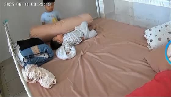 Big brother watches over baby sister in bed while mom tidies up in Kuala Lumpur, Malaysia