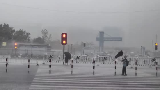 Boy struggles against strong winds and heavy rain while crossing street in Guangxi, China