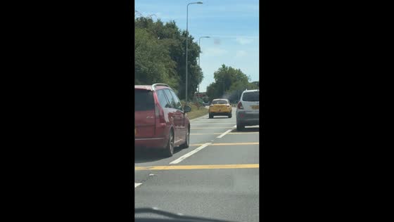 Yellow car with a wagging tail travels on highway in Sandy, England, UK