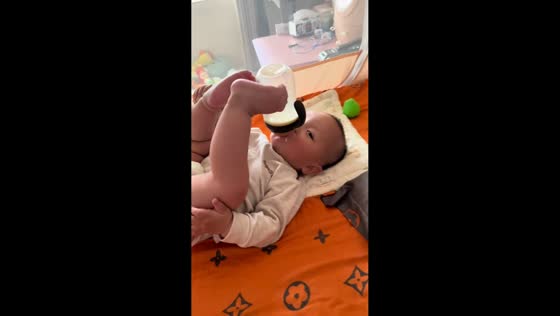 Toddler drinks milk while holding bottle with feet in Zhejiang, China