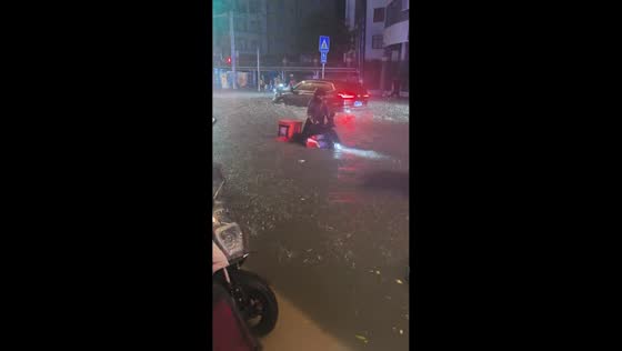 People push motorcycle through flooded street during heavy rain in Guangdong, China