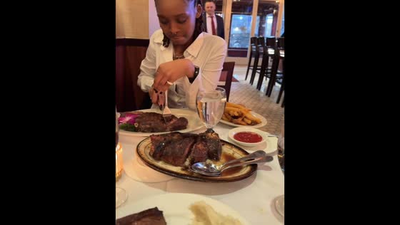 Friend struggles to cut steak on a shaky table in New York, USA