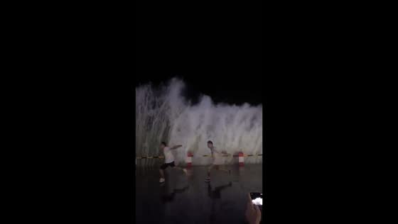Two men perform synchronized jump moves as wave crashes in Guangxi