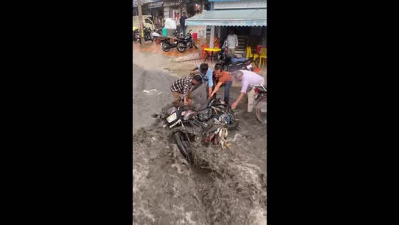 Motorcycle held by people to prevent flood sweep in Hyderabad