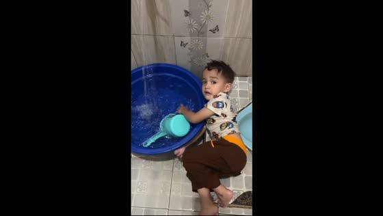 Little boy lies beside basin and plays with running water in Bekasi, Java, Indonesia