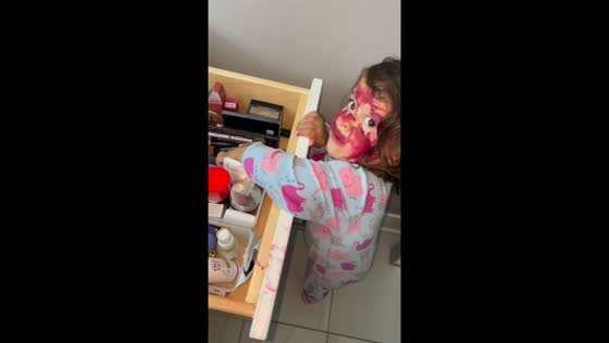 Little girl paints her face with lipstick in Prairie Village, Kansas, USA