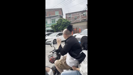 Man struggles to keep his wig in place while riding an e-bike in Fujian, China