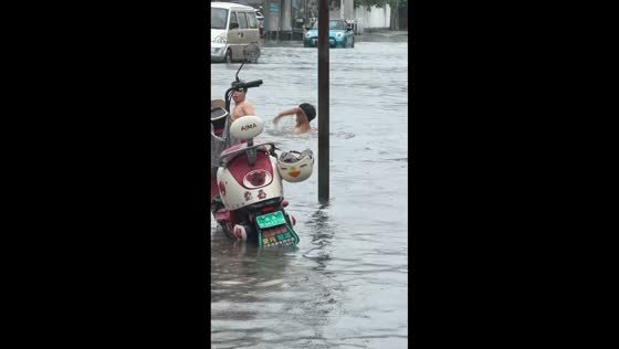 Two men swim near submerged motorcycle as woman walks through floodwaters in Jiangsu, China