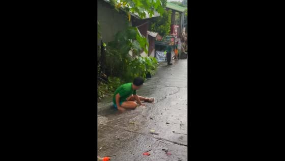People sliding down slippery street in the rain in Laguna, Philippines