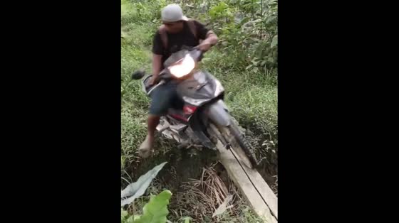 A man riding a motorcycle fell on a thin wood bridge in Indonesia