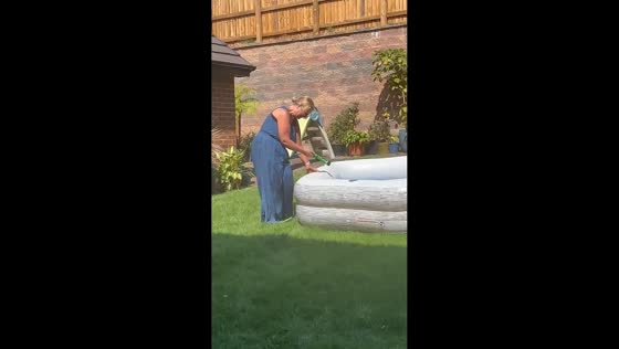 Woman struggles to control runaway garden hose while filling paddling pool in England, UK