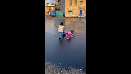 Siblings break through frozen puddle while playing in Leninskoye, Russia