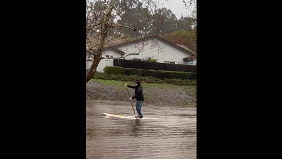 A man uses paddleboards in the flood area of Goleta.