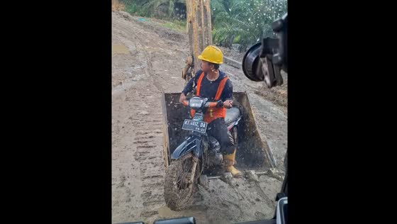 Rescuing a worker on a motorcycle from the mud by excavator arm in East Kalimantan