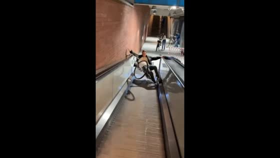 Man loses balance and tumbles with bicycle on flat escalator in Tilburg, Netherlands