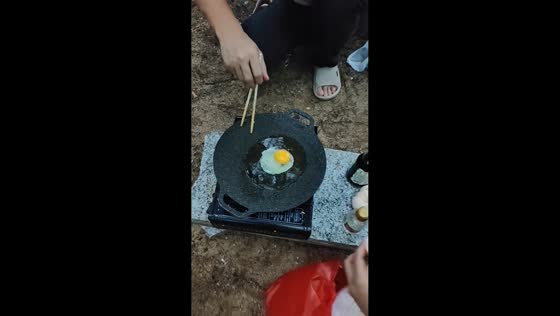 Boy throws sand into fried rice while family cooks outdoors in Guangxi, China