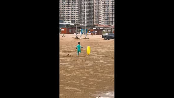 Boy chases windblown yellow donut floater along beach in Shandong, China