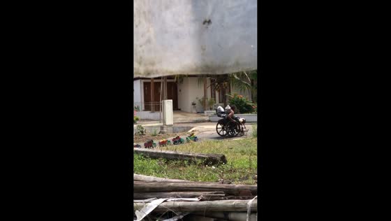 Grandfather rides wheelchair with toy trucks on slope in Sleman, Yogyakarta