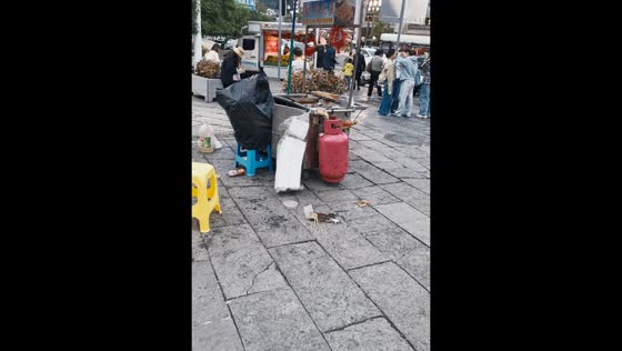 Street food vendor wears garbage bag while sitting behind stall in Guizhou, China