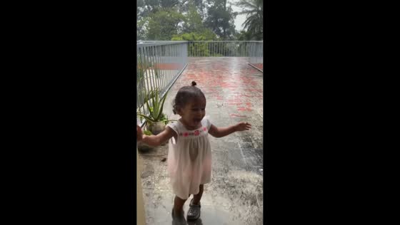 Toddler plays excitedly on balcony during rain in La Vega, Dominican Republic