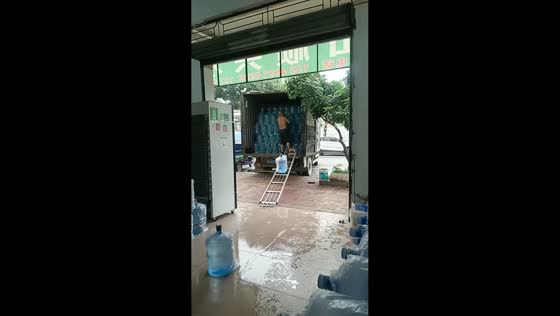 Delivery worker slides water jugs down ramp during unloading in Guangdong, China