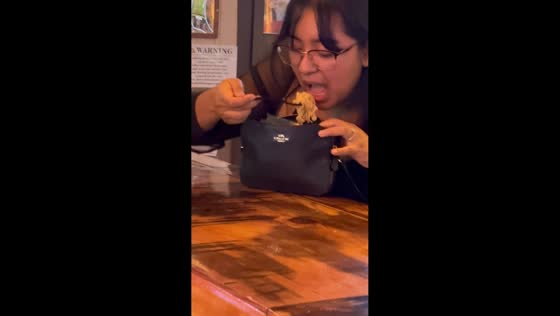 Woman eats noodles from purse at bar in Marysville, California, USA