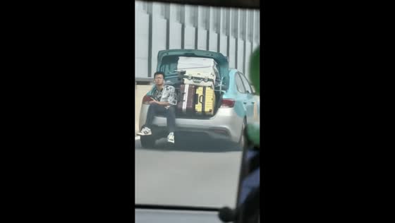 Man rides in open trunk of luggage-packed sedan, Guangzhou, China