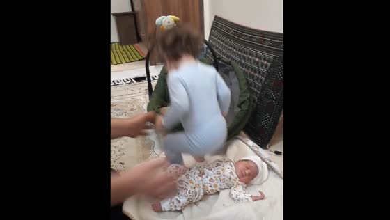 Toddler tries to sit on newborn sibling in Iran