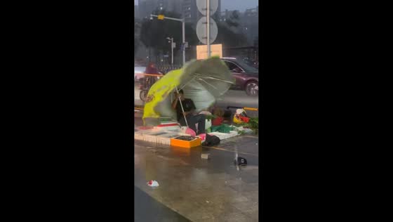 Vendor holds onto umbrella during heavy storm in Guangdong, China
