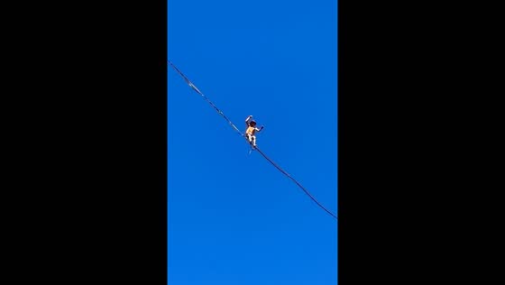 Slackliner balances above rocks while dirt bikers navigate below