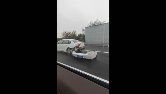 Car drives along a highway with a broken rear bumper dragging behind in Jiangsu, China