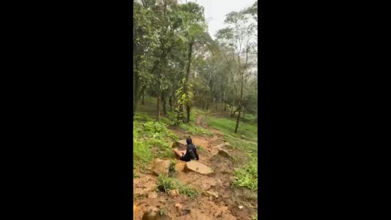 Two men slip on muddy trail during hike in East Java, Indonesia