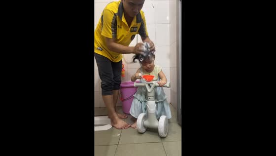Father washes daughter’s hair while she rides toy bike in Guangdong, China