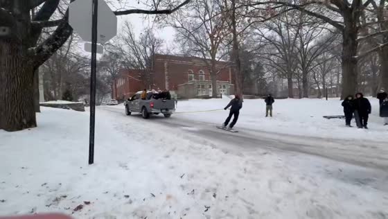 Snowboarder towed behind pickup on snowy road in Athens, Ohio, USA